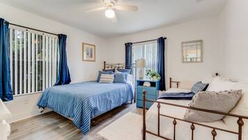 A bedroom with a bed, a nightstand, a dresser, a ceiling fan, and a window with curtains.