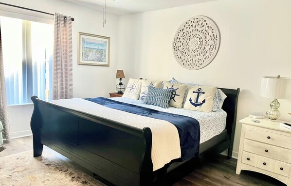 A bedroom with a bed, a bedside table, a lamp, a wall decoration, and a window with curtains. - Family Welcome-Large Comfy Stay Pets Welcome w/Parking Trailers/Bikes/Boats (Edgewater)