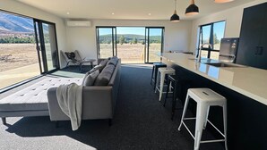A modern kitchen with a large window, a sofa, and a dining area. - Manuka Vista | under the stars getaway in Twizel (Mackenzie District)