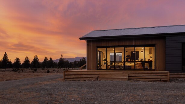 A modern house with a large glass door, a wooden deck, and a view of the surrounding landscape. - Manuka Vista | under the stars getaway in Twizel (Mackenzie District)
