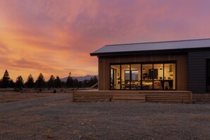 Una casa moderna con un amplio ventanal, una terraza de madera y vistas del paisaje circundante.