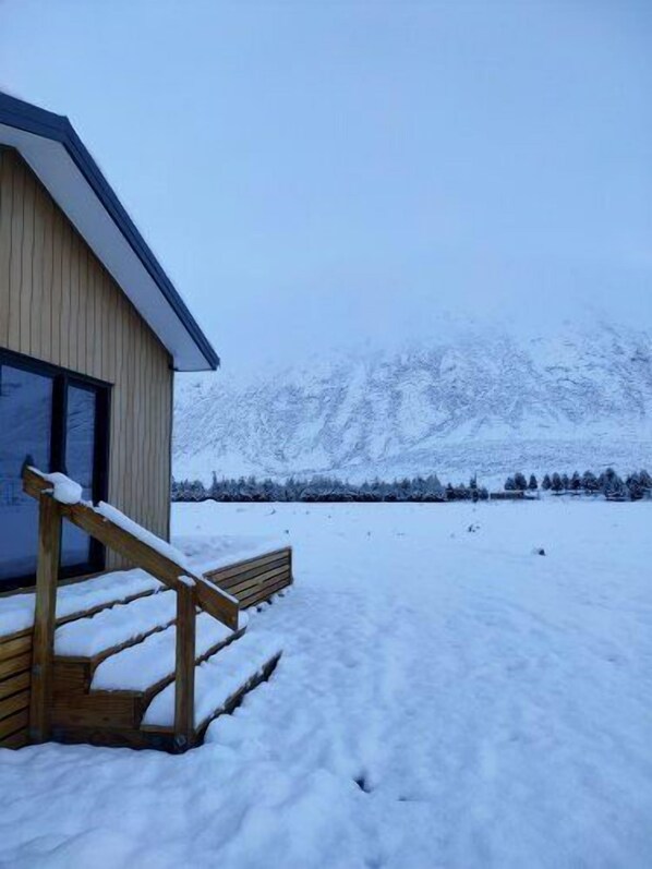 Un banco de madera frente a un edificio, con un paisaje nevado y montañas al fondo.