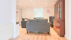 Uma sala de estar moderna com um sofá cinzento, piso de madeira, um armário e uma televisão.
