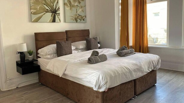 A neatly made bed with white linens, a brown headboard, and a pair of rolled towels on the side.