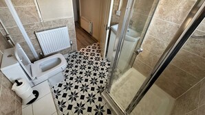 A bathroom with a toilet, bidet, shower, and tiled floor.