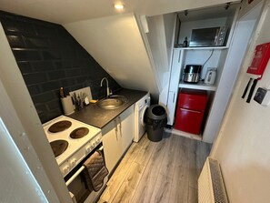 A compact kitchen with a stove, sink, and a red refrigerator.