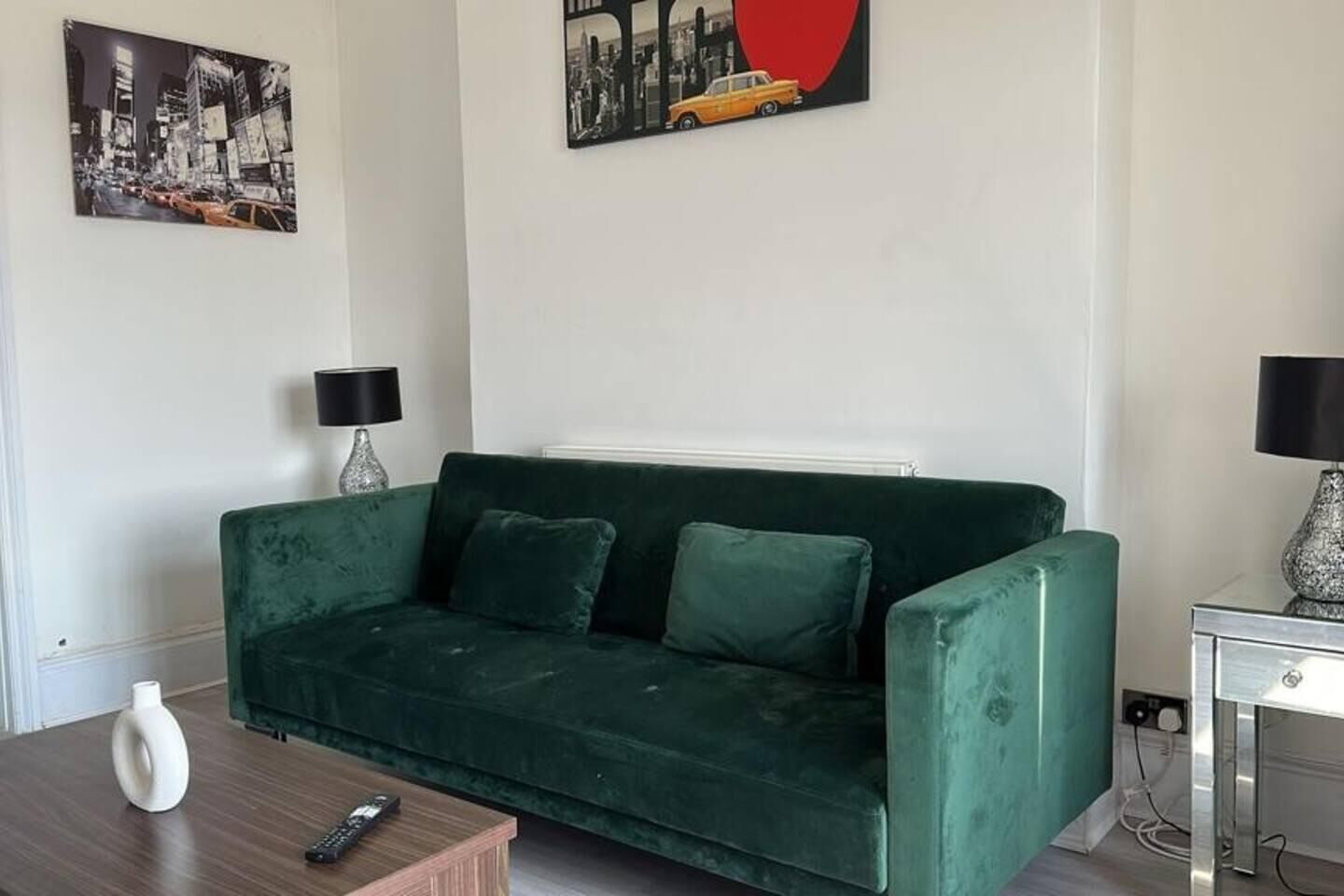 A green sofa in a living room with a remote control on a wooden side table.