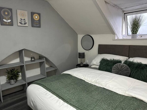 A bedroom with a bed, a bedside table, a lamp, a shelf with a plant, and three wall art pieces.