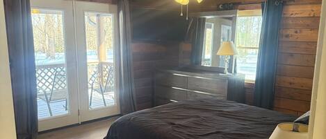 Un dormitorio con cama, cómoda, lámpara y ventilador de techo. Hay una puerta corrediza de vidrio que da a un espacio exterior con patio y sillas.