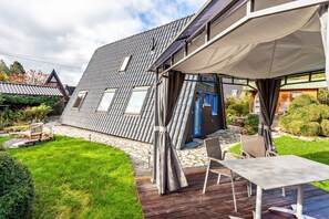A modern house with a sloped roof, a patio with a table and chairs, and a blue door. - Holiday Home 'Villa Natura' with Mountain View, Terrace, Garden & Wi-Fi (Meschede)