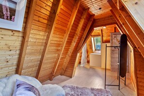 Un dormitorio en el ático con vigas de madera, una cama con un almohadón mullido, un aparador y un refrigerador.