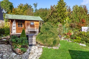 Une cabane en bois avec un sentier de pierres menant à un banc, le tout entouré d’un jardin bien entretenu.