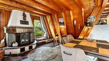L’intérieur d’une cabane en rondins, avec une cheminée en pierre, des poutres en bois au plafond, une table à manger et un coin salon confortable.