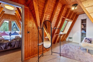 Une pièce en bois aux hauts plafonds, comprenant un lit, un miroir, un canapé blanc et une bibliothèque.