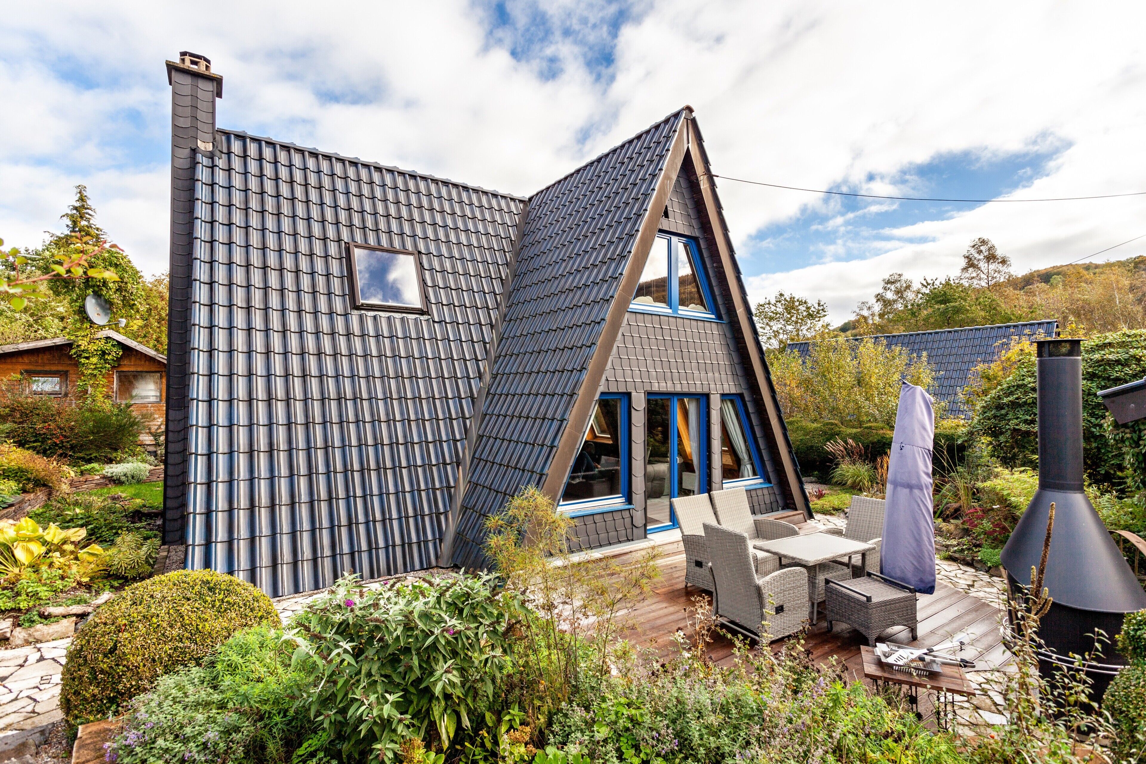 A modern house with a sloped roof, a chimney, and a patio with outdoor furniture.