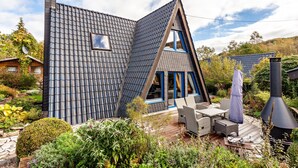 Une maison moderne avec un toit en pente, une cheminée et un patio aménagé avec du mobilier d’extérieur.