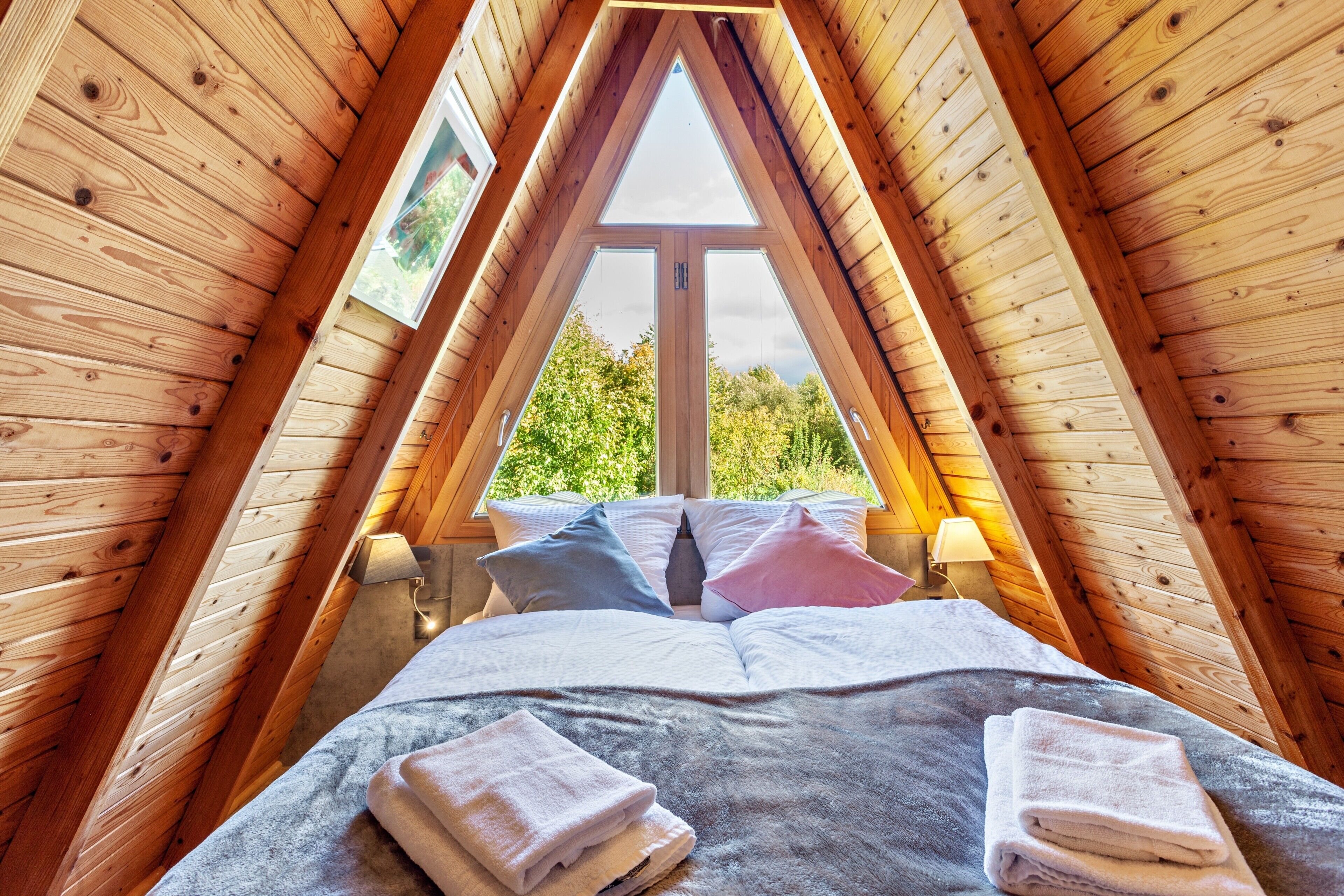 A bedroom with a sloped ceiling, a large window, and a bed with pillows and towels.