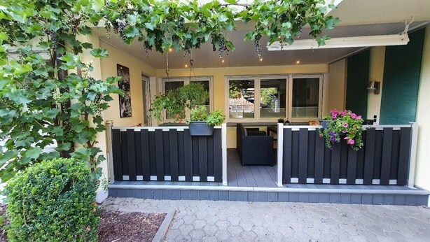 Un patio techado con cerca negra, plantas en macetas y vista a la calle.