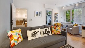 Una sala de estar moderna con un sofá gris, cojines coloridos, un sillón gris y una mesita auxiliar.