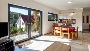 A modern kitchen with sliding glass doors, a dining area with a table and chairs, and a television on a stand.