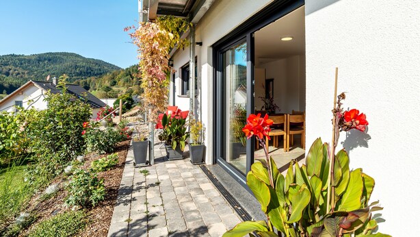 A residential property with a paved patio, potted plants, and a view of a hillside.