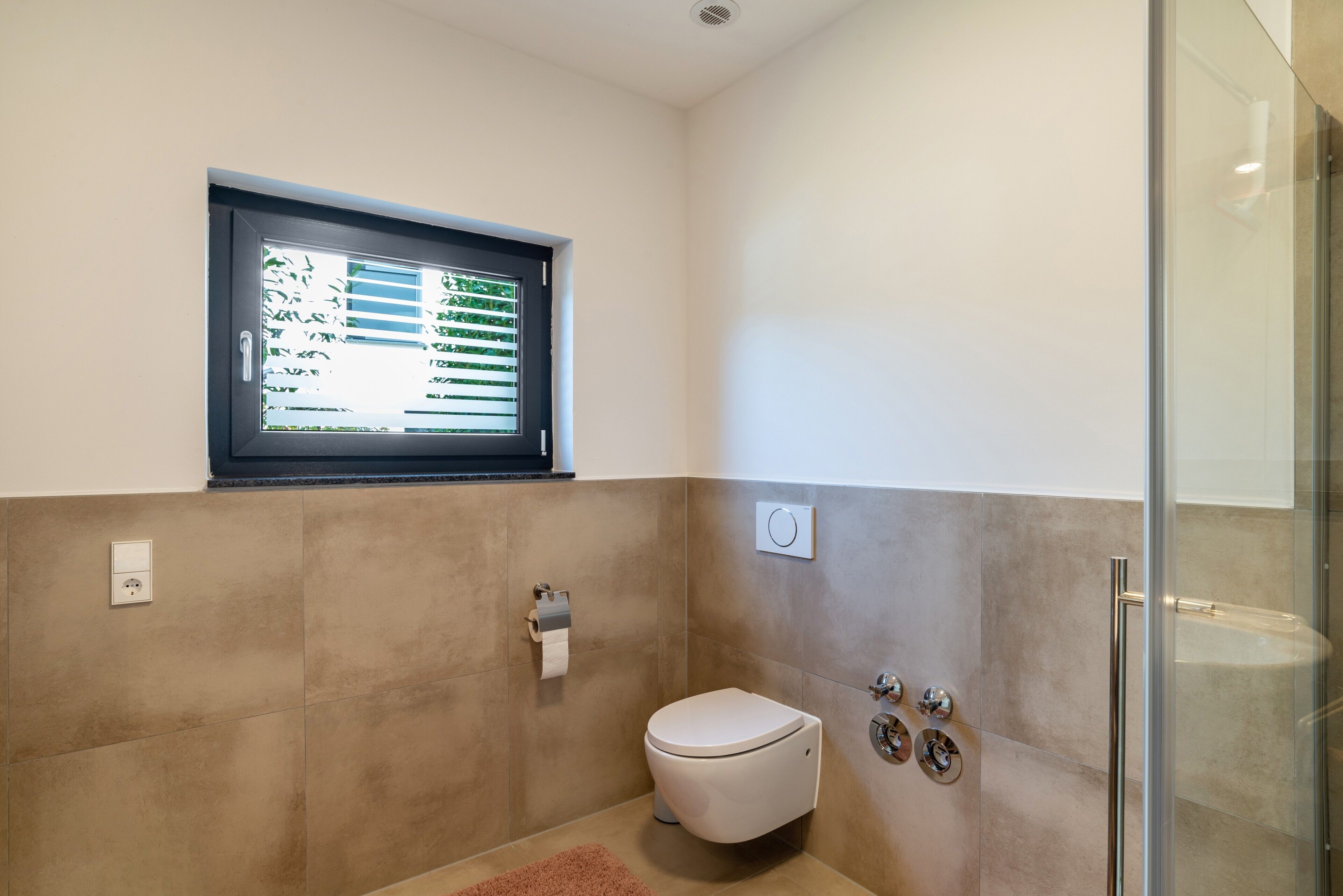 Une salle de bain équipée de toilettes, d’une fenêtre, d’une douche et d’un distributeur de serviettes.