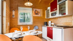 Ein Holzblockhaus-Innenraum mit einem Esstisch für zwei Personen, einer Küche mit einem roten Kühlschrank und einem Fenster mit Blick auf Bäume.