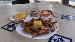 Une table à manger dressée avec un repas composé de riz, de crevettes frites et d’une salade, le tout mis en valeur par un décor comprenant une piscine et des palmiers.