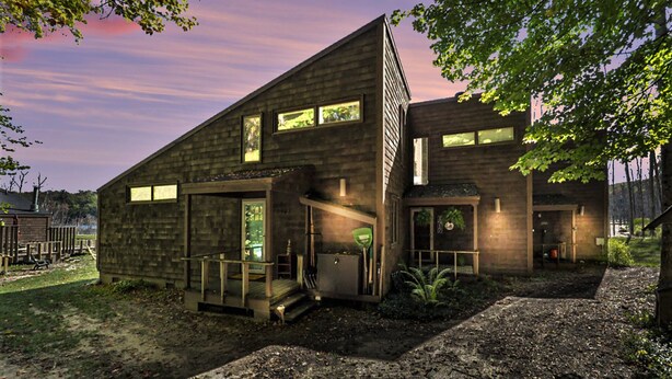 A modern two-story building with large windows, a covered outdoor area, and a dirt path leading to the entrance.