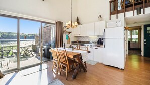 A spacious kitchen with a large dining table, wooden chairs, and a view of the sea through large sliding glass doors.