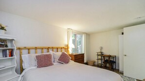 A bedroom with a bed, a nightstand, a desk, and a bookshelf.