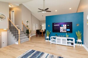 A modern living room with a staircase, a flat-screen TV mounted on a blue wall, and a wooden floor.