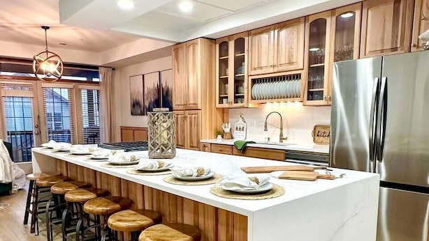 A modern kitchen with a central island, bar stools, wooden cabinets, and a stainless steel refrigerator. - SKI IN/OUT- Pool table, hot tub, A+ kitchen, 7 bedrooms->4 kings+custom kid rms! (Snowshoe)