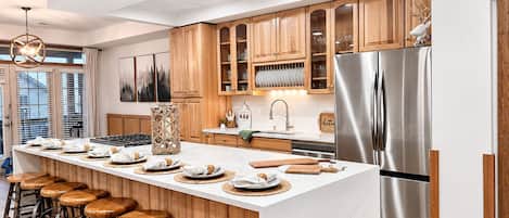 A modern kitchen with a central island, wooden cabinets, stainless steel appliances, and bar stools.