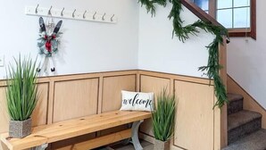 A staircase with a wooden handrail, a bench with a 'welcome' sign, a coat rack with hooks, and a decorative wall with a deer head and greenery. - SKI IN/OUT- Pool table, hot tub, A+ kitchen, 7 bedrooms->4 kings+custom kid rms! (Snowshoe)