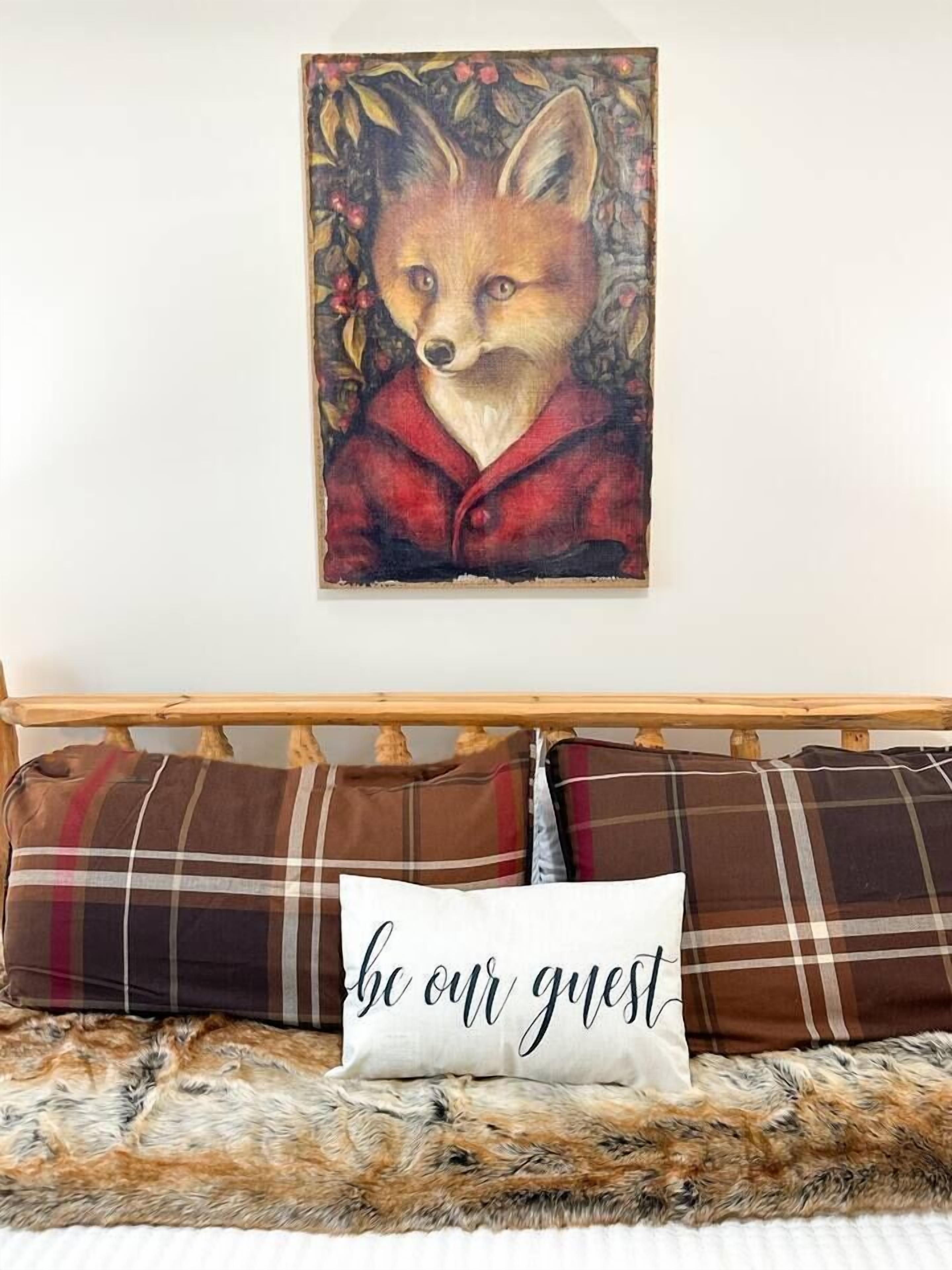 A bed with a fur throw, plaid pillows, and a wall-mounted fox painting.
