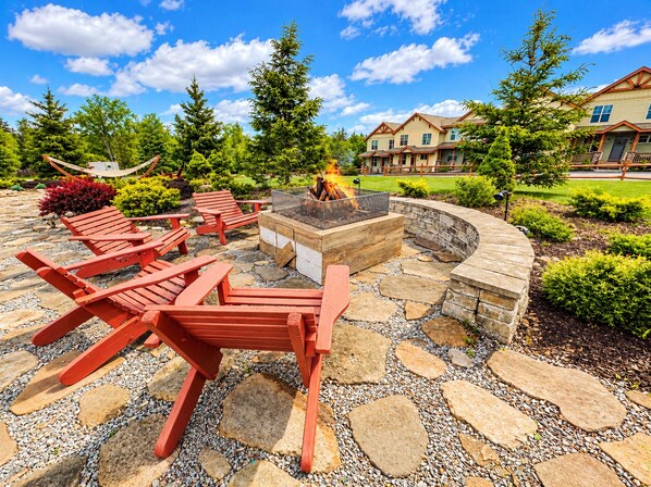 A patio area with a fire pit, red Adirondack chairs, and a stone pathway.