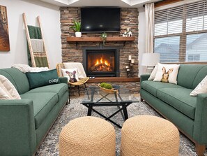 A living room with green sofas, a fireplace, a flat-screen TV, and a patterned rug. - SKI IN/OUT- Pool table, hot tub, A+ kitchen, 7 bedrooms->4 kings+custom kid rms! (Snowshoe)