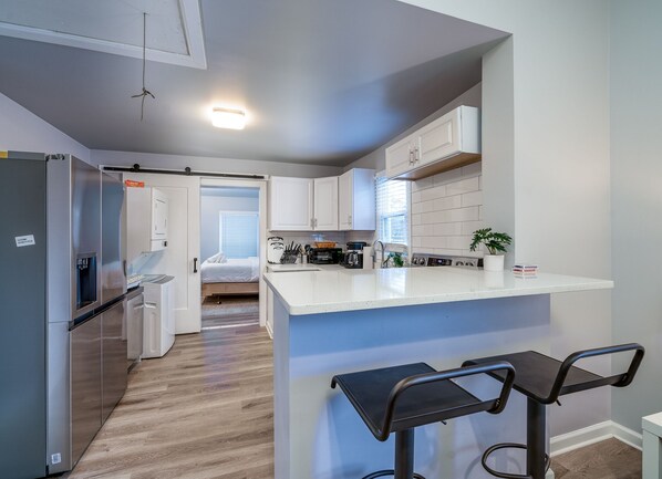 A modern kitchen with a central island, white cabinetry, and a small seating area with two stools.