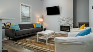 A modern living room with a grey sofa, white armchair, and a small white coffee table. A flat-screen TV is mounted on the wall above the fireplace. - 3 Bedroom 3 Bath House  in Atlanta -Two Blocks To GWCC, Mercedes-Benz Stadium  (Atlanta)