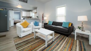 A modern living room with a grey sofa, two white armchairs, a white coffee table, and a colorful striped rug. There is a kitchen in the background with white cabinets and a dining area. - 3 Bedroom 3 Bath House  in Atlanta -Two Blocks To GWCC, Mercedes-Benz Stadium  (Atlanta)