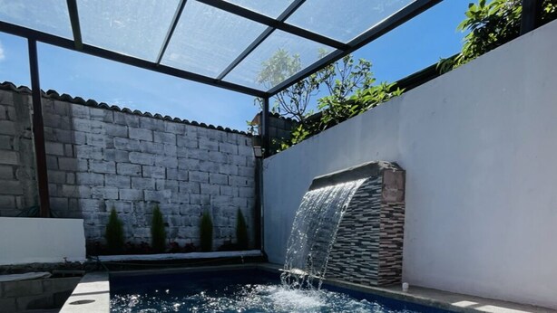A swimming pool with a waterfall feature, surrounded by a white wall and a glass enclosure. - A Magical Place just Minutes away from the most Beautiful View of Cuenca.  (Cuenca)