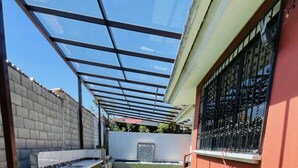 A covered patio area with artificial green turf, a stone bench, and a window with decorative iron bars. - A Magical Place just Minutes away from the most Beautiful View of Cuenca.  (Cuenca)
