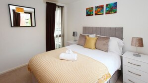 Ein Hotelzimmer mit einem großen Bett, einem Nachttisch mit Lampe, einem Spiegel und drei farbenfrohen Bildern an der Wand.