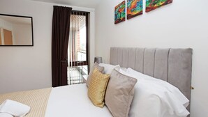 Ein Hotelzimmer mit Bett, einem fensterbelaubten Fenster, einem Wandspiegel und zwei Wandbildern.
