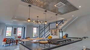 Een moderne keuken met een centraal eiland, roestvrijstalen apparatuur en hangende lampen.