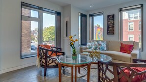 Een moderne woonkamer met grote ramen, een glazen salontafel, een bank en een decoratief bord.