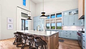 A modern kitchen with a large island, light blue cabinets, and a bar stool area. - 283 Lakeview Drive (Seagrove Beach)