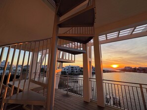Un balcone con vista sul tramonto sull'acqua, ringhiere in legno e una scala.
