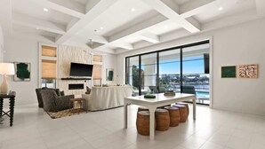 A spacious living area with a white ceiling, a flat-screen TV mounted above a fireplace, a dining table with stools, and a large window offering a city view. - 283 Lakeview Drive (Seagrove Beach)